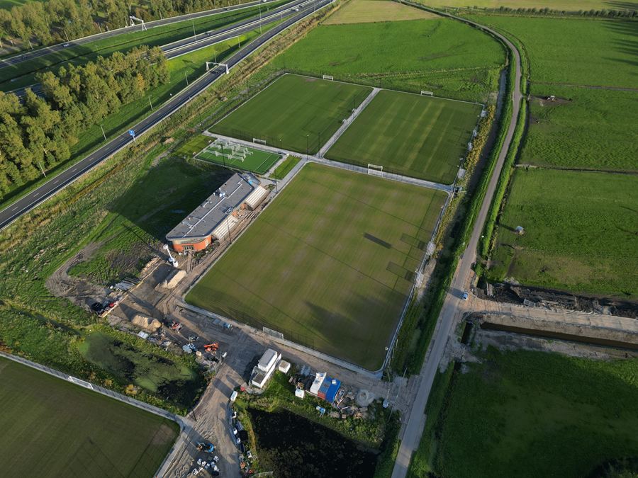 Het hoofdveld en het clubhuis schuin van boven, met de weg en weilanden eromheen