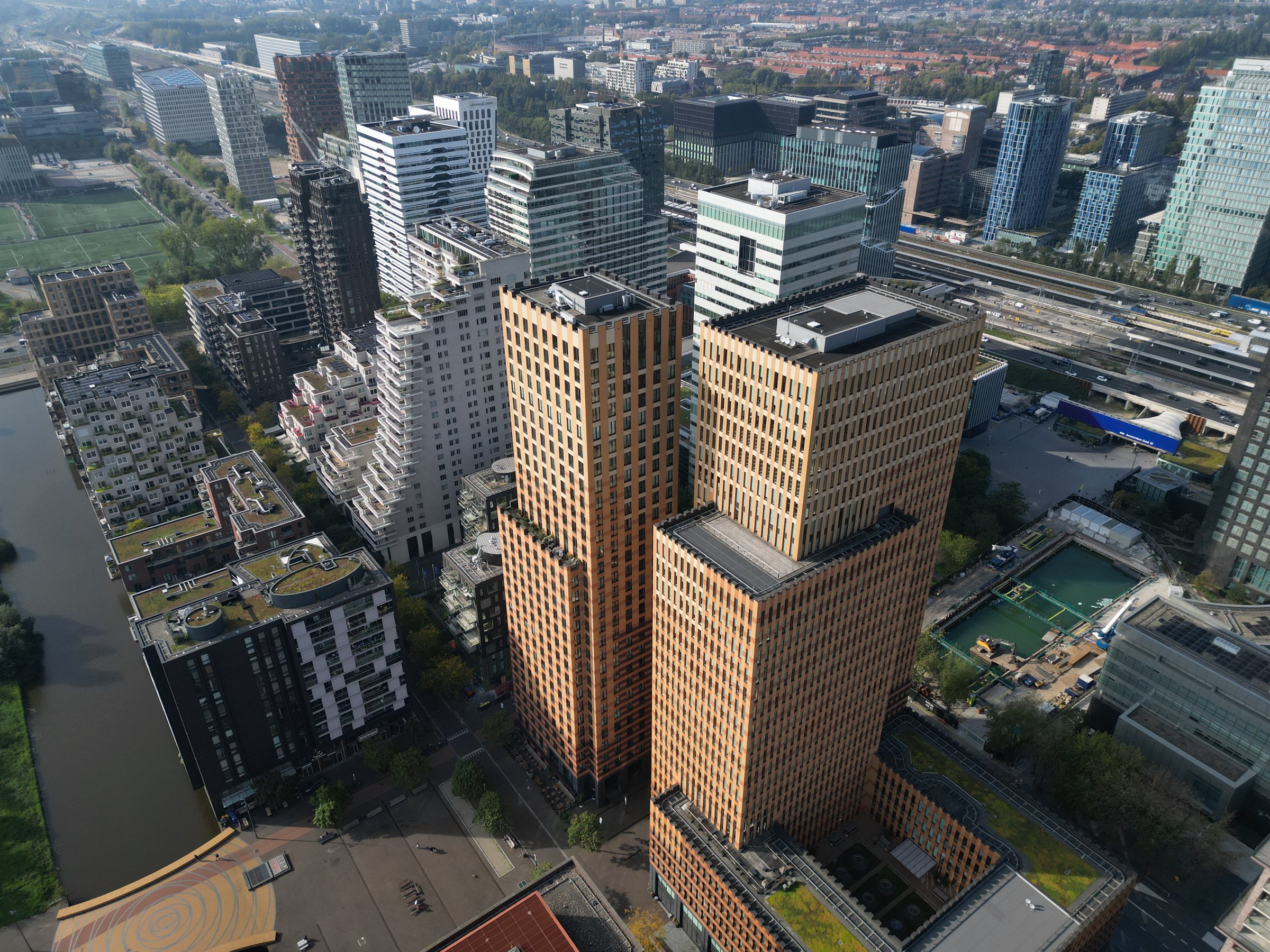 Luchtfoto van kantoortorens in een stedelijk gebied, met woontorens, water en infrastructuur eromheen